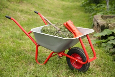 Photo of Wheelbarrow with mown grass, rubber boots and pitchfork outdoors