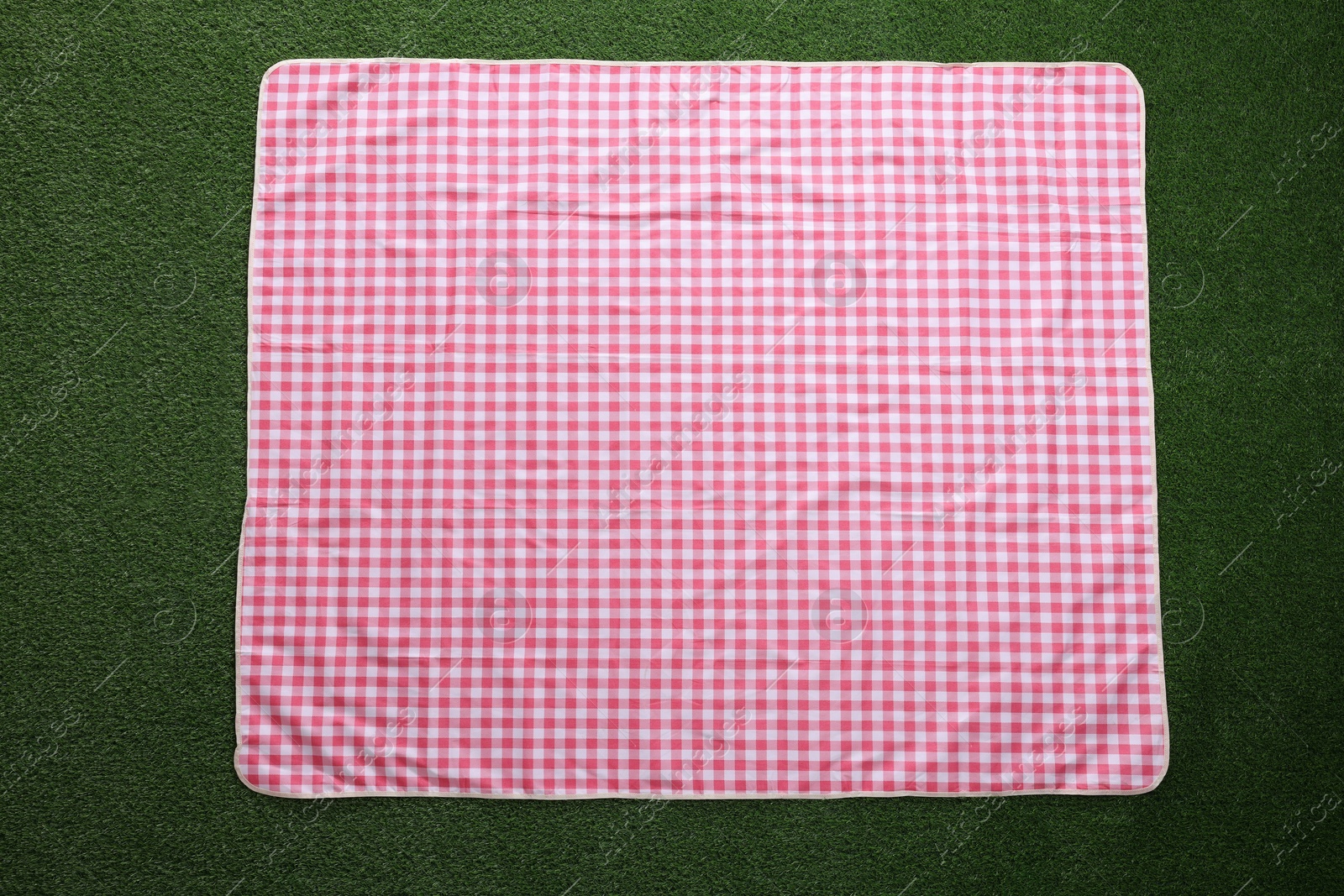 Photo of Checkered picnic tablecloth on green grass, top view