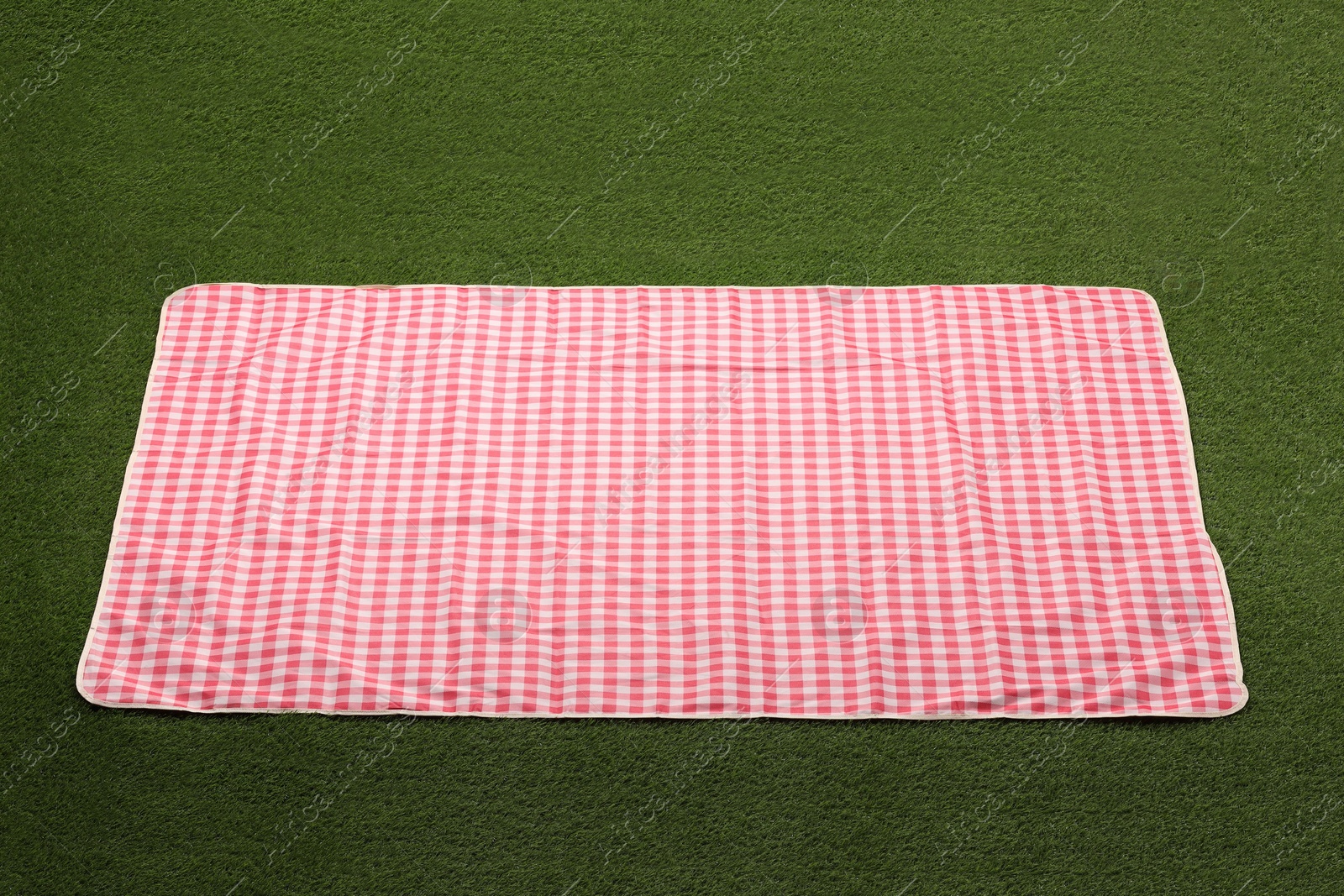 Red checkered picnic tablecloth on green grass Photo of Red checkered picnic tablecloth on green grass