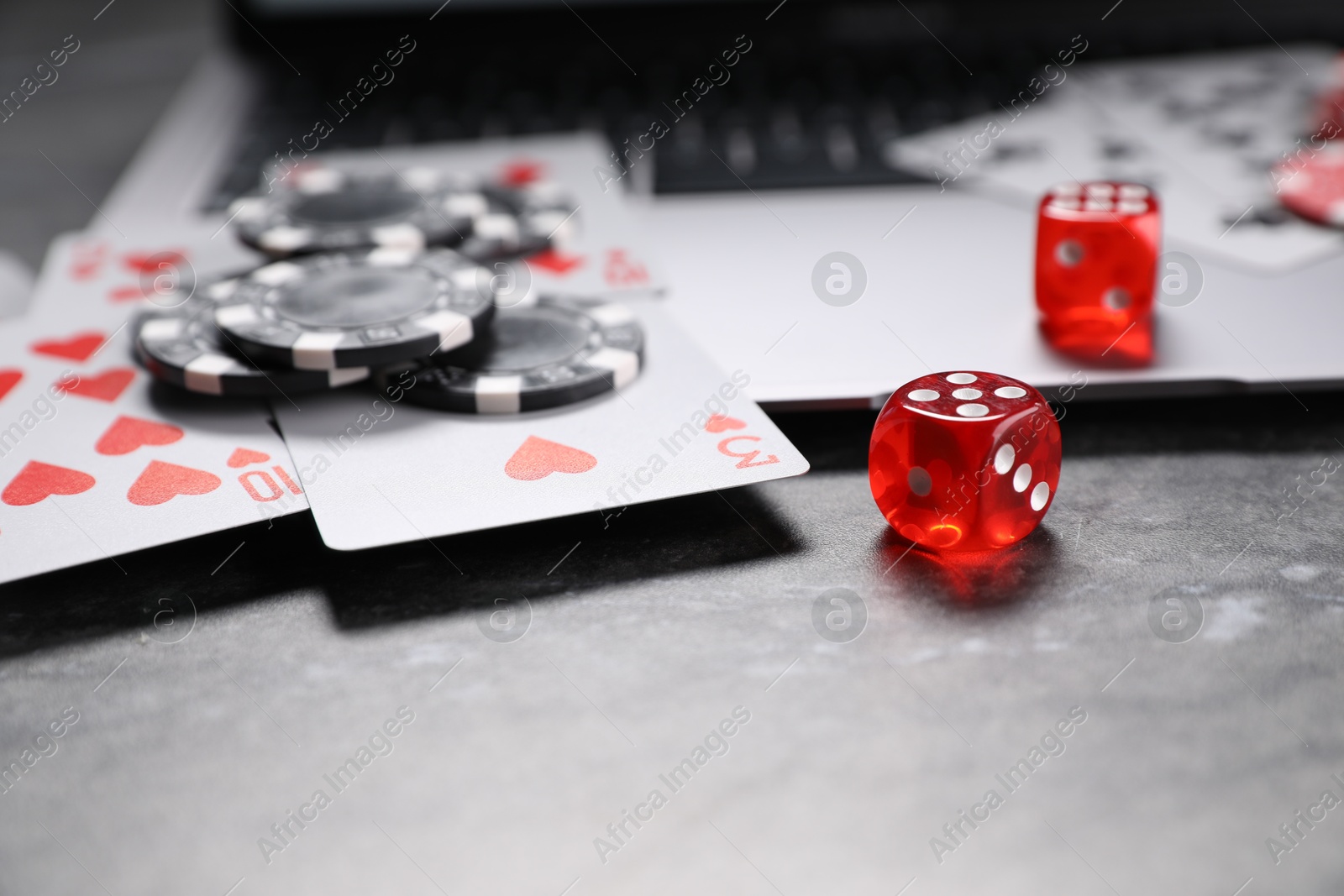 Photo of Poker chips, laptop, playing cards and dices on grey table, closeup. Online game