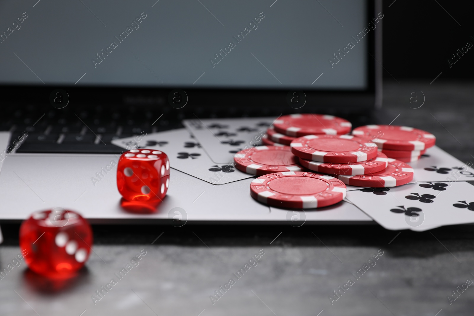 Photo of Poker chips, laptop, playing cards and dices on grey table, closeup. Online game