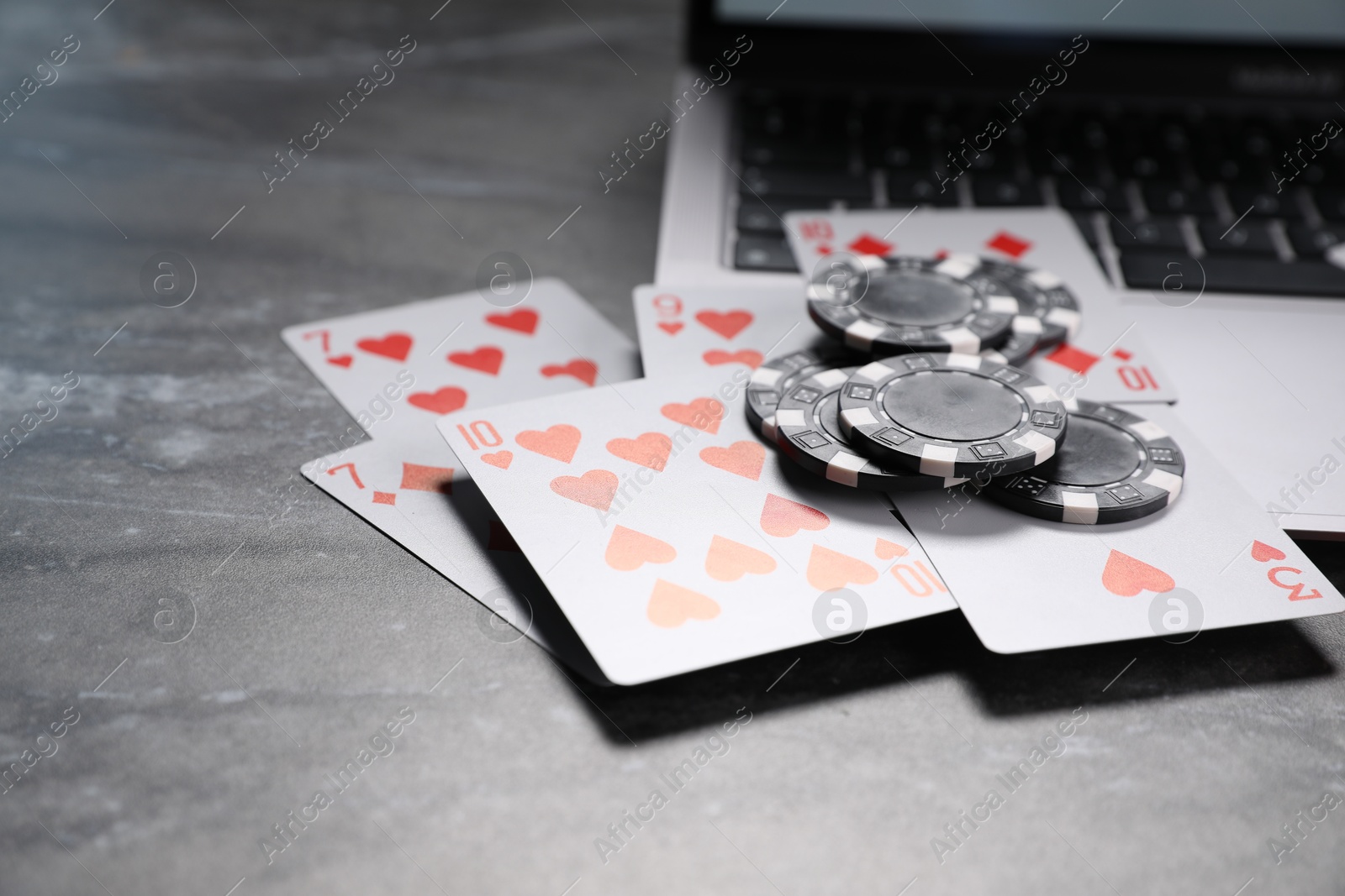 Photo of Poker chips, laptop and playing cards on grey textured table, closeup. Online game