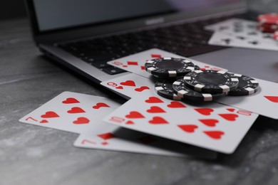 Photo of Poker chips, laptop and playing cards on grey table, closeup. Online game