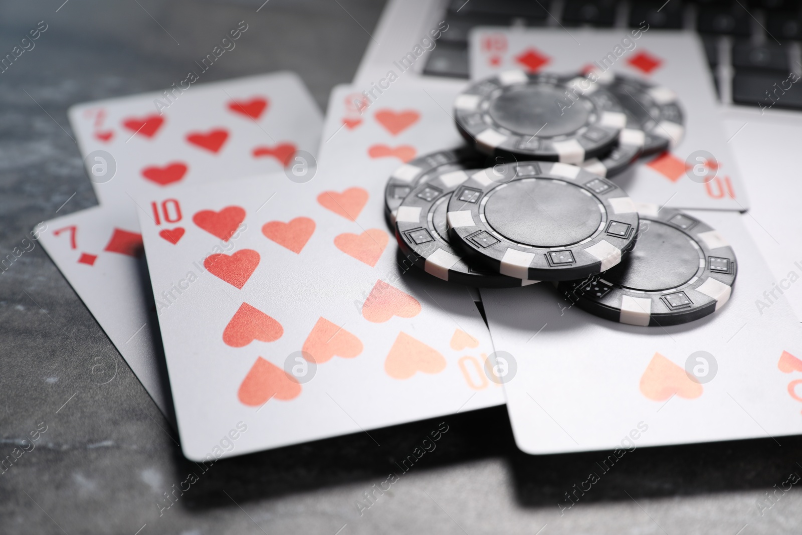 Photo of Poker chips, laptop and playing cards on grey table, closeup. Online game