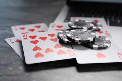 Photo of Poker chips, laptop and playing cards on grey table, closeup. Online game