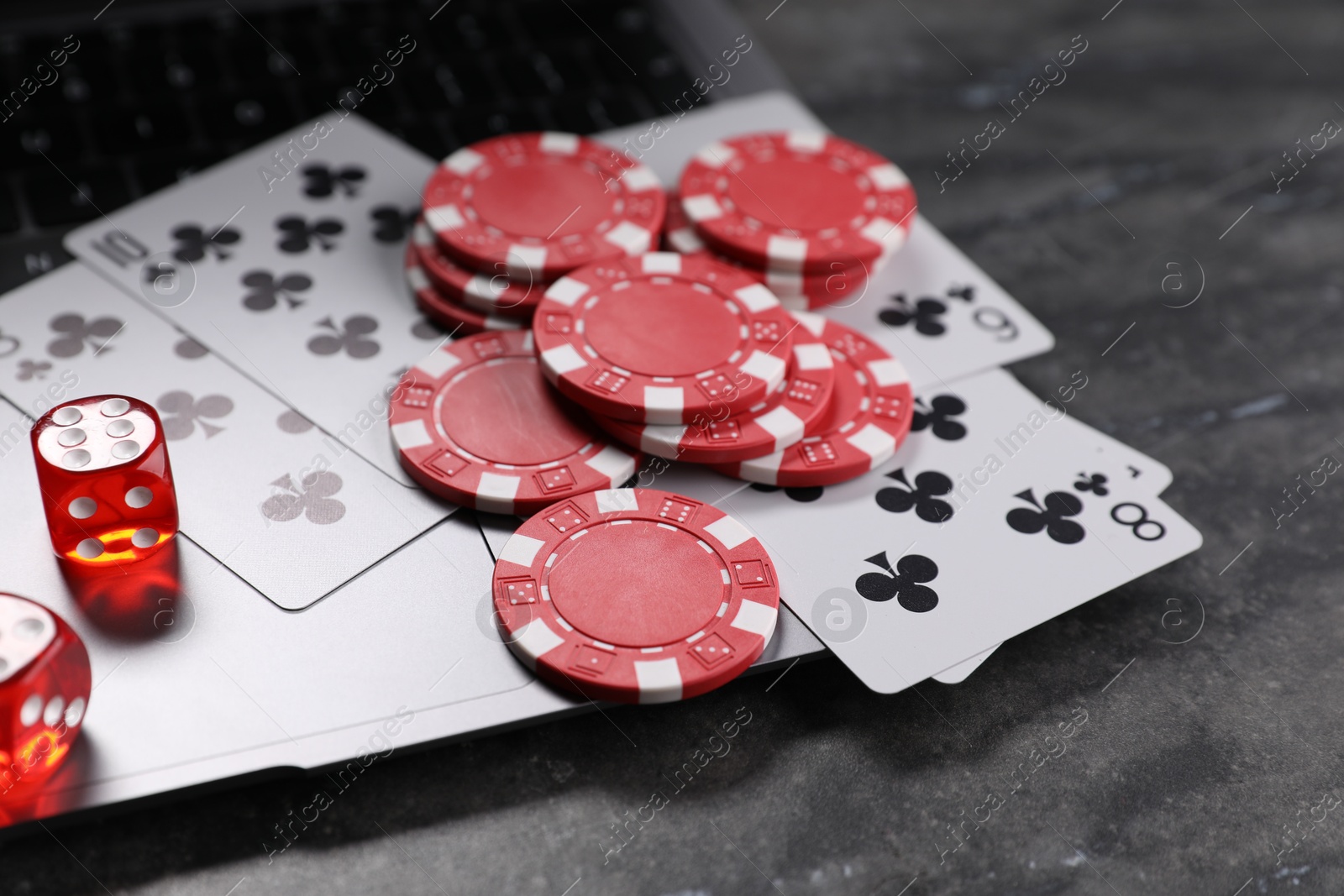 Photo of Poker chips, laptop, playing cards and dices on grey textured table, closeup. Online game