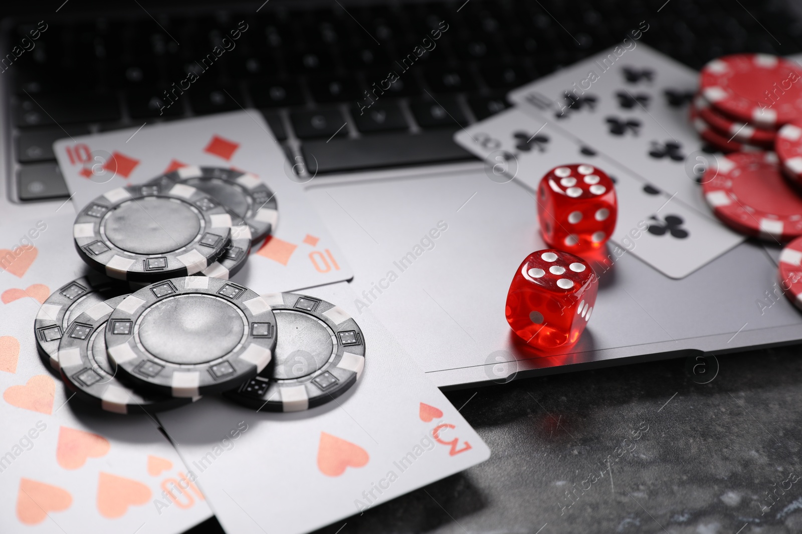 Photo of Poker chips, laptop, playing cards and dices on grey table. Online game