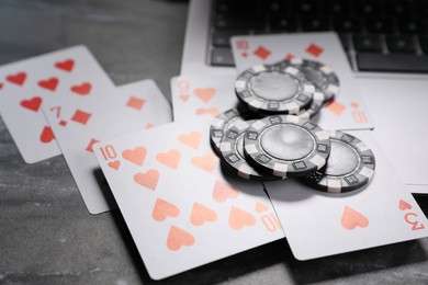 Photo of Poker chips, laptop and playing cards on grey table, closeup. Online game