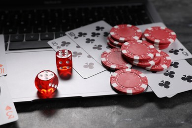 Photo of Poker chips, laptop, playing cards and dices on grey table. Online game