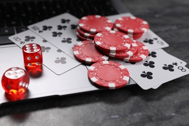 Photo of Poker chips, laptop, playing cards and dices on grey table, closeup. Online game