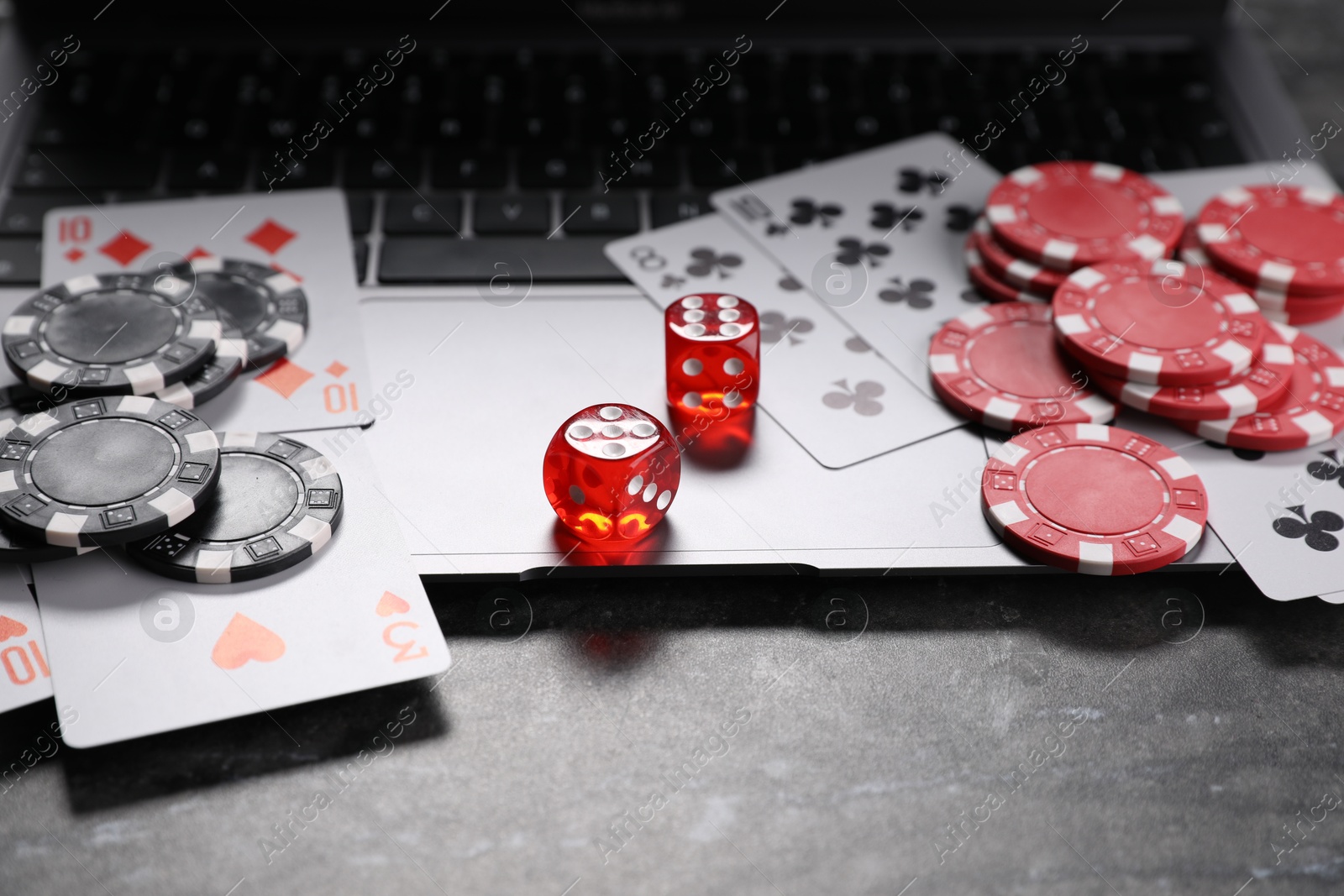 Photo of Poker chips, laptop, playing cards and dices on grey table. Online game