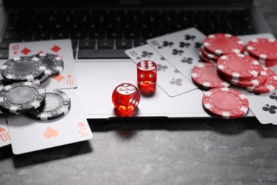 Photo of Poker chips, laptop, playing cards and dices on grey table. Online game