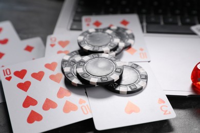 Photo of Poker chips, laptop and playing cards on grey table, closeup. Online game