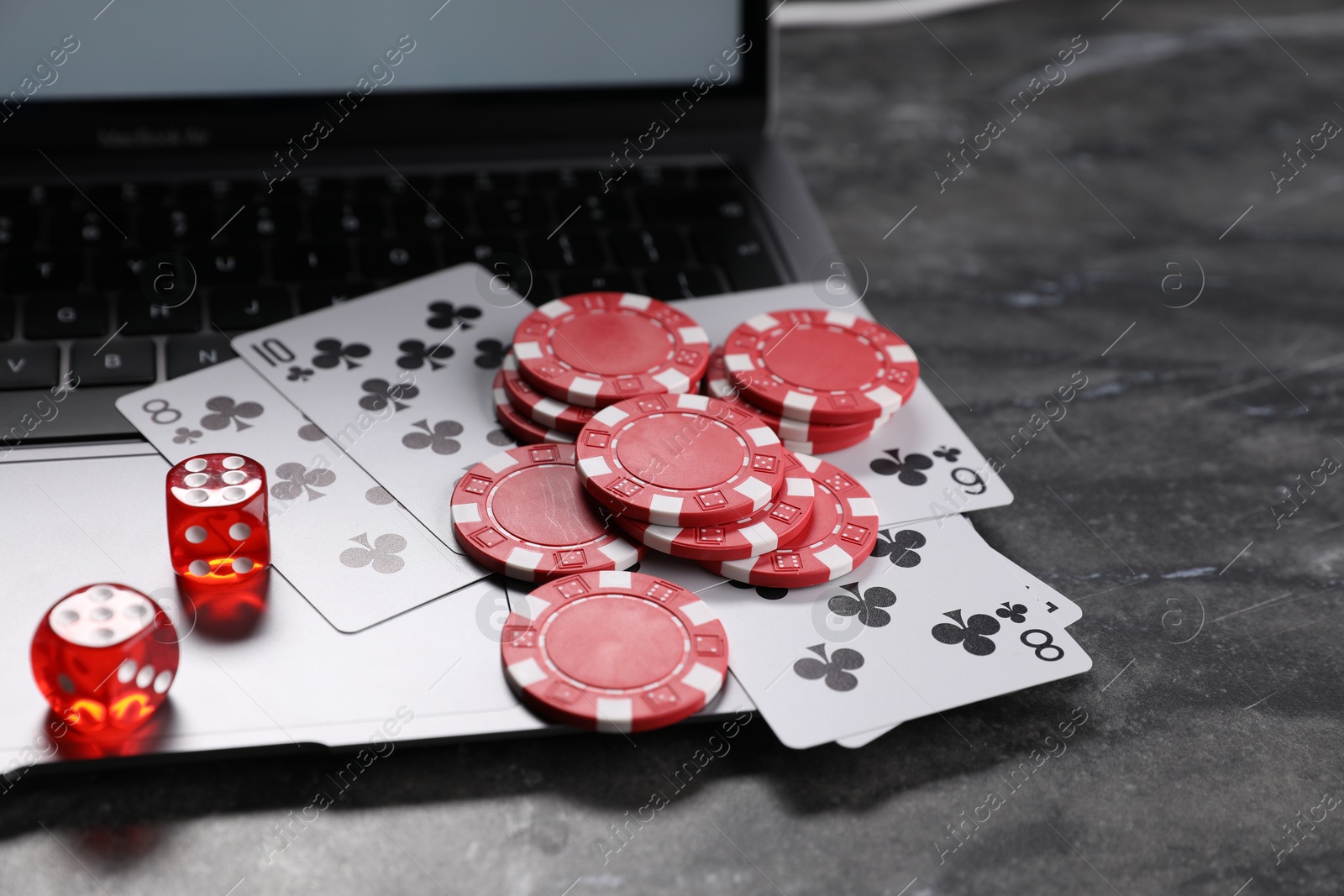 Photo of Poker chips, laptop, playing cards and dices on grey table. Online game