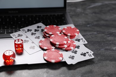 Photo of Poker chips, laptop, playing cards and dices on grey table. Online game