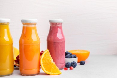 Glass bottles of tasty smoothies and different products on white table, space for text