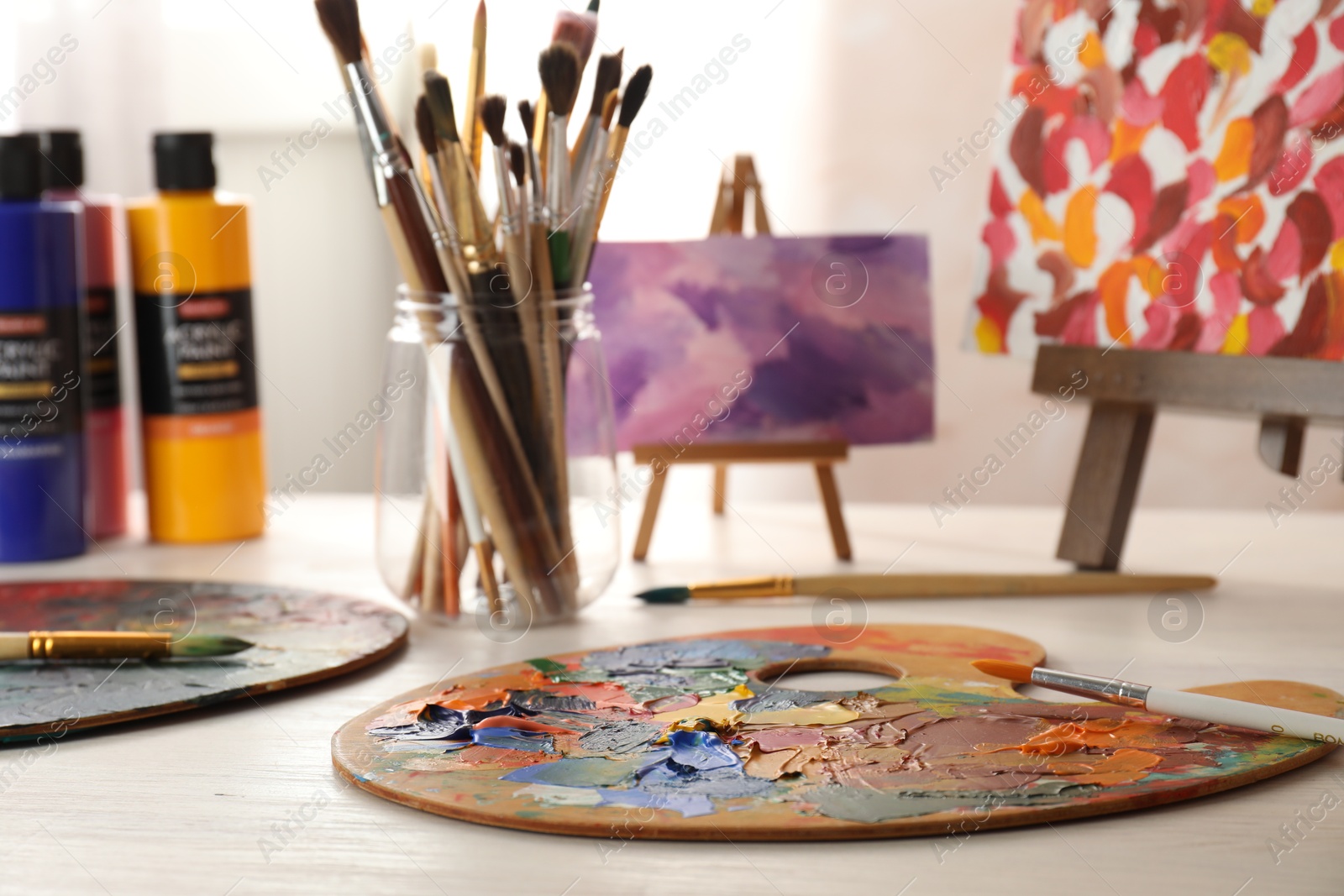 Photo of Artist's palette with mixed paints, brushes and small easels on wooden table indoors