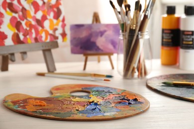 Photo of Artist's palette with mixed paints, brushes and small easels on wooden table indoors