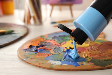 Photo of Woman mixing paints on palette at wooden table indoors, closeup