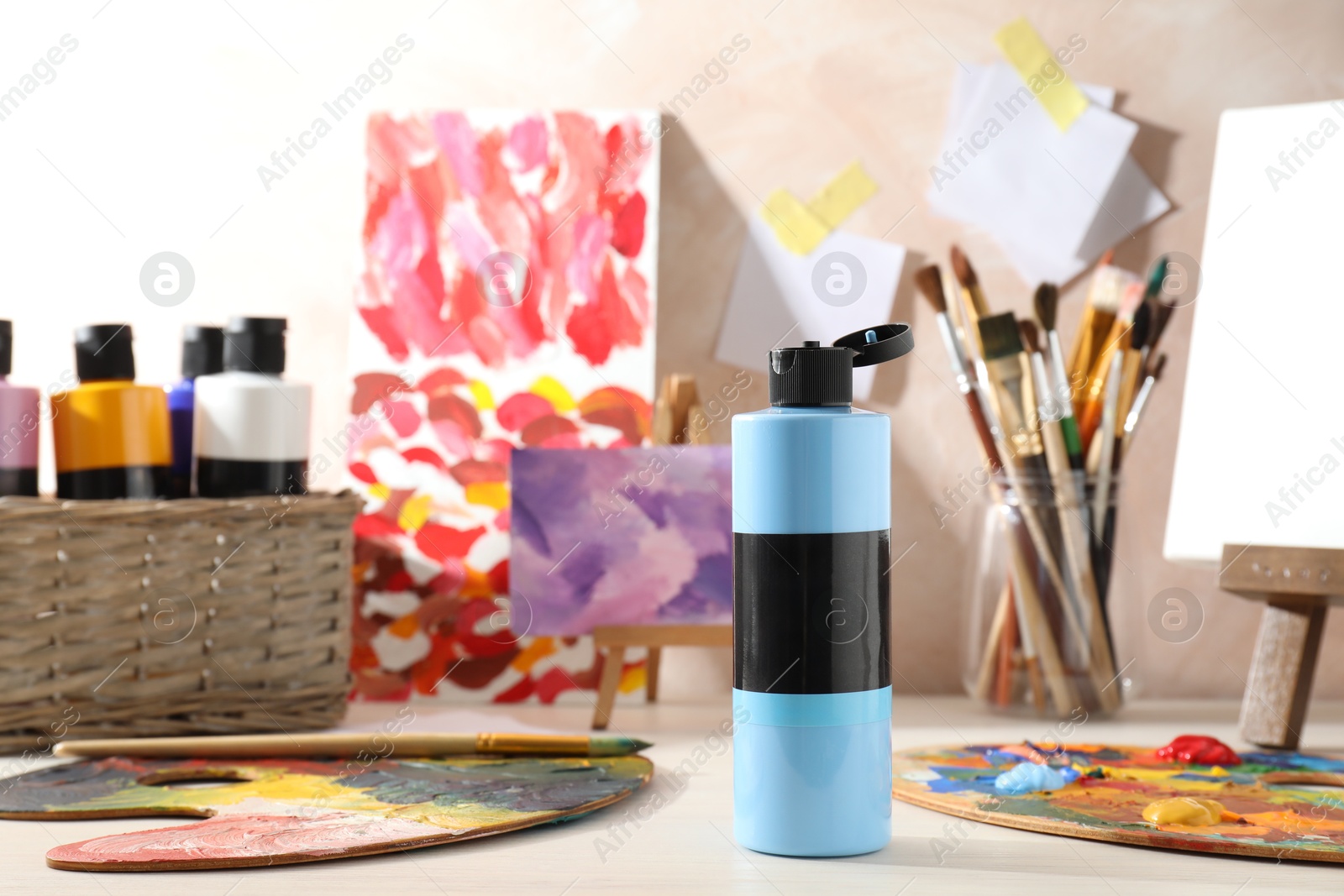 Photo of Blue acrylic paint in bottle, small easels, palettes and brushes on wooden table indoors