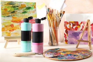 Photo of Acrylic paints of different colors, palette, knife, brushes and small easel with abstract picture on wooden table