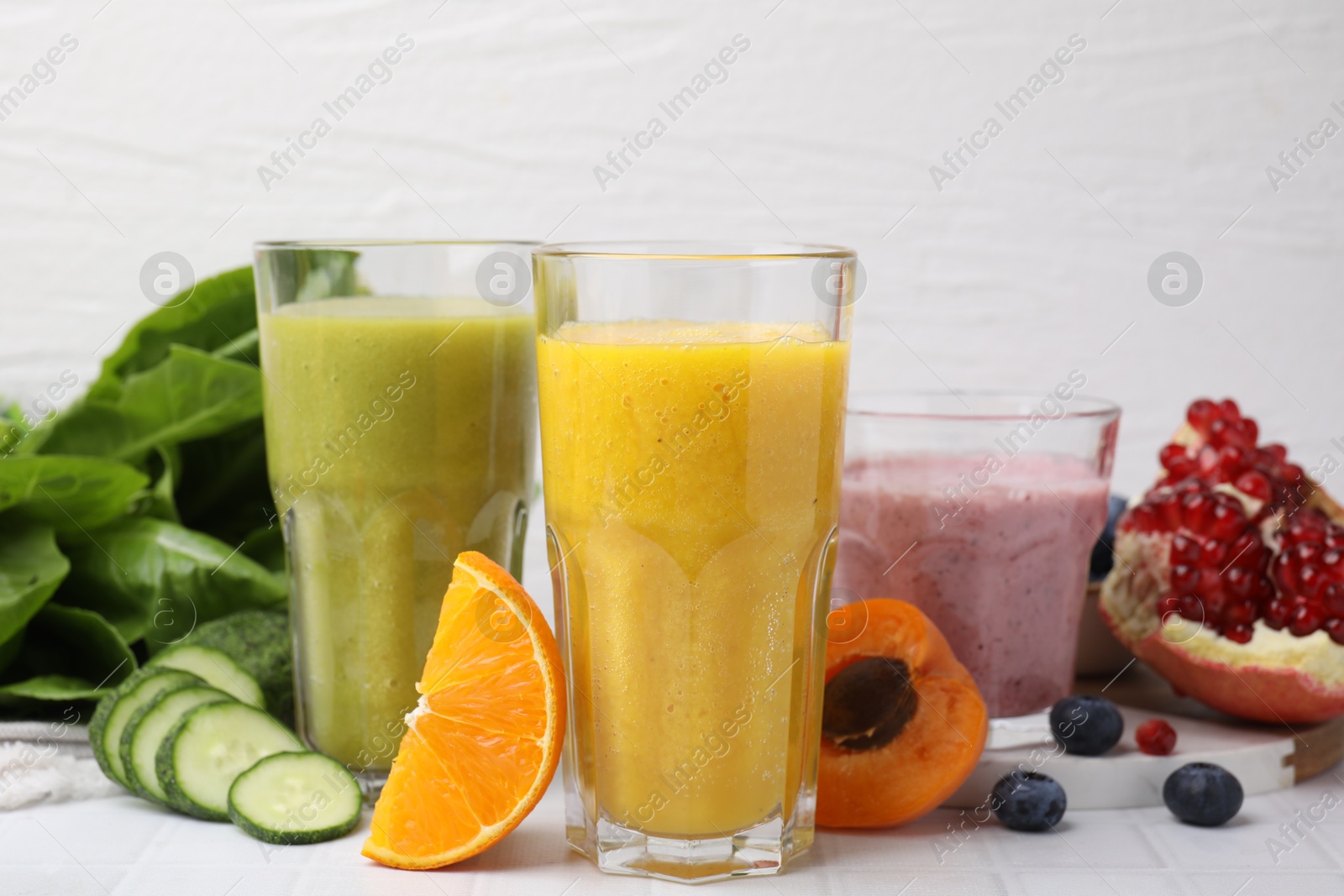 Photo of Tasty smoothies in glasses and ingredients on white tiled table, closeup