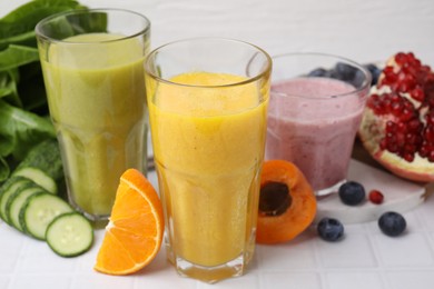 Tasty smoothies in glasses and ingredients on white tiled table, closeup