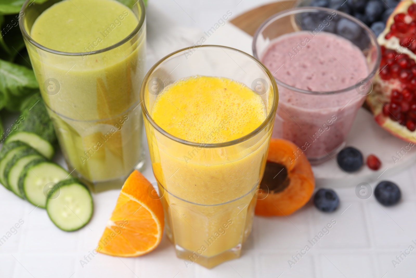 Photo of Tasty smoothies in glasses and ingredients on white tiled table, closeup