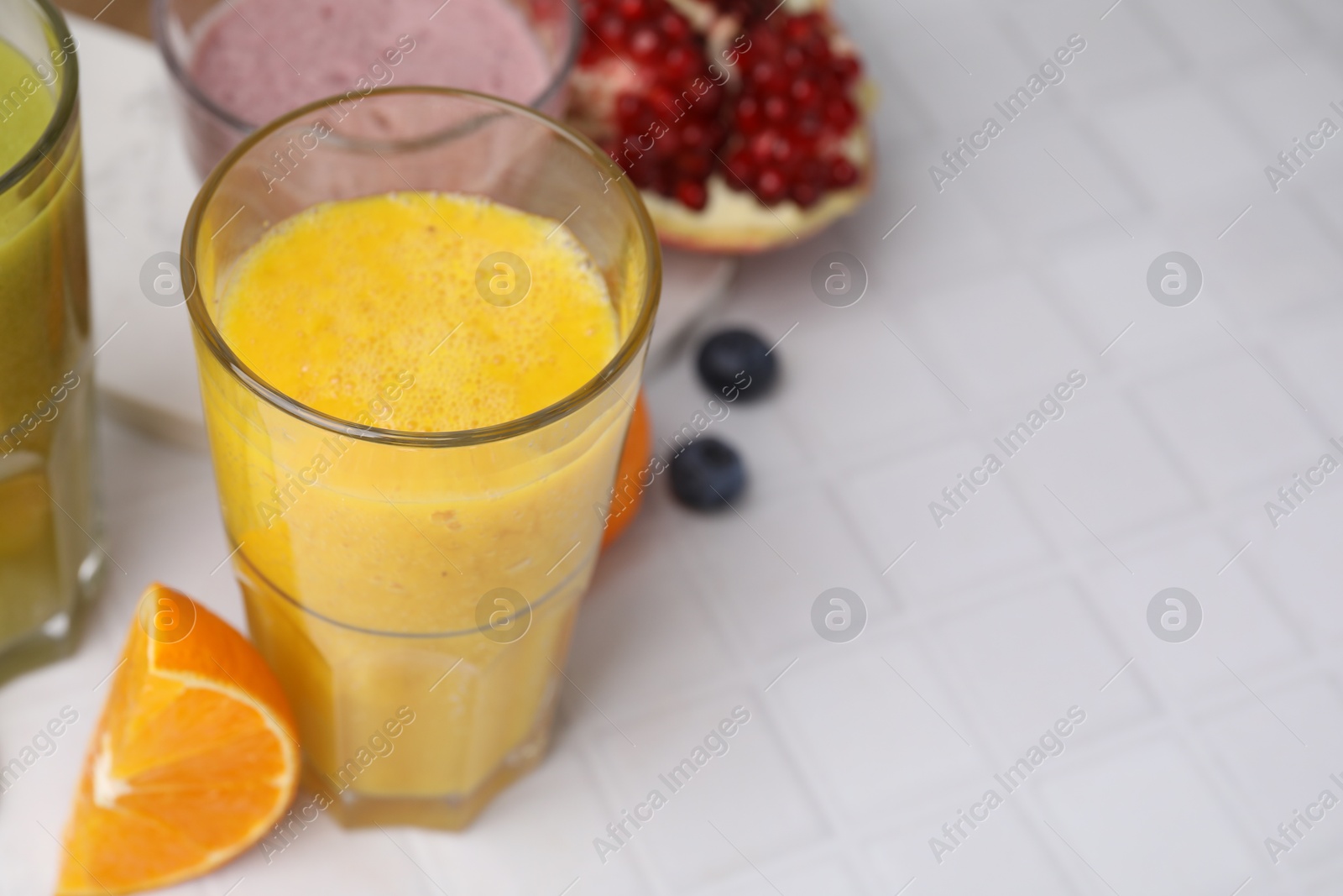 Photo of Tasty smoothies in glasses and ingredients on white tiled table, closeup. Space for text