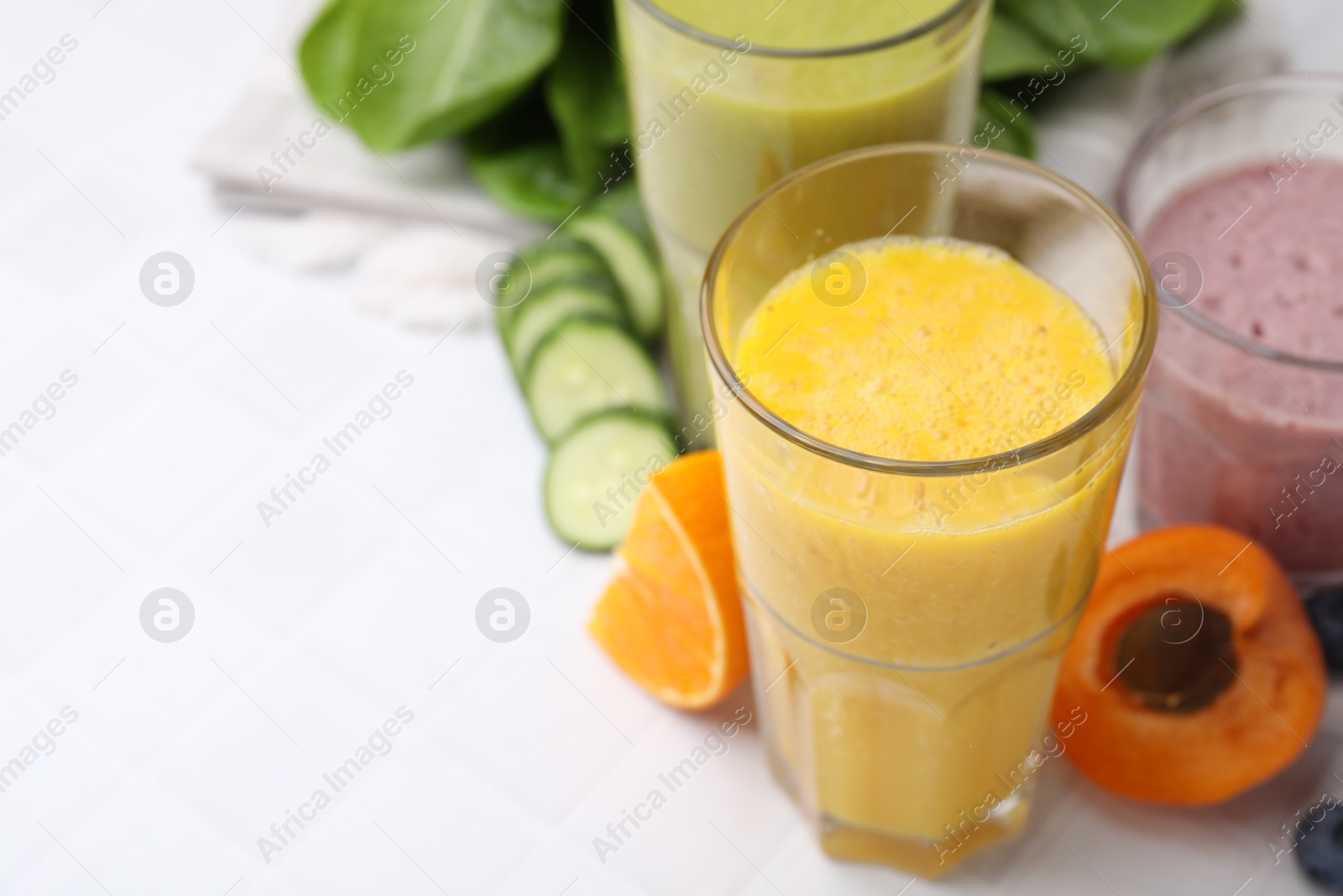 Photo of Tasty smoothies in glasses and ingredients on white tiled table, closeup. Space for text