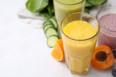 Tasty smoothies in glasses and ingredients on white tiled table, closeup. Space for text