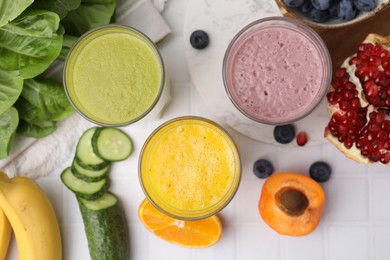 Tasty smoothies in glasses and ingredients on white tiled table, flat lay