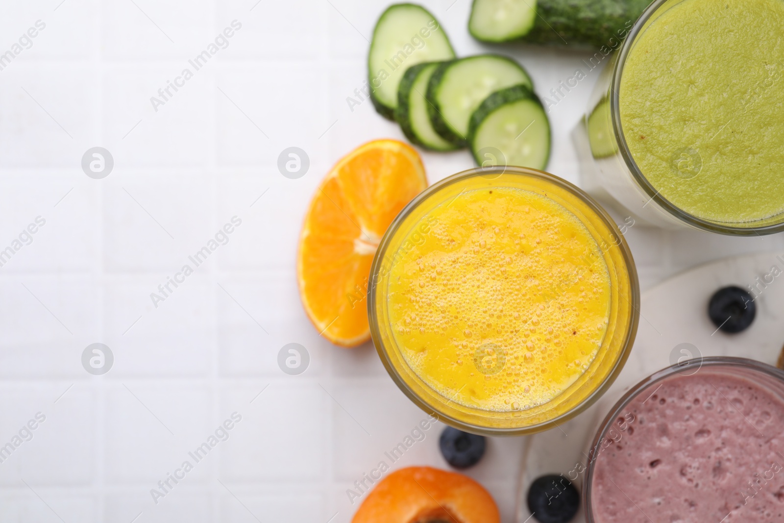 Photo of Tasty smoothies in glasses and ingredients on white tiled table, flat lay. Space for text