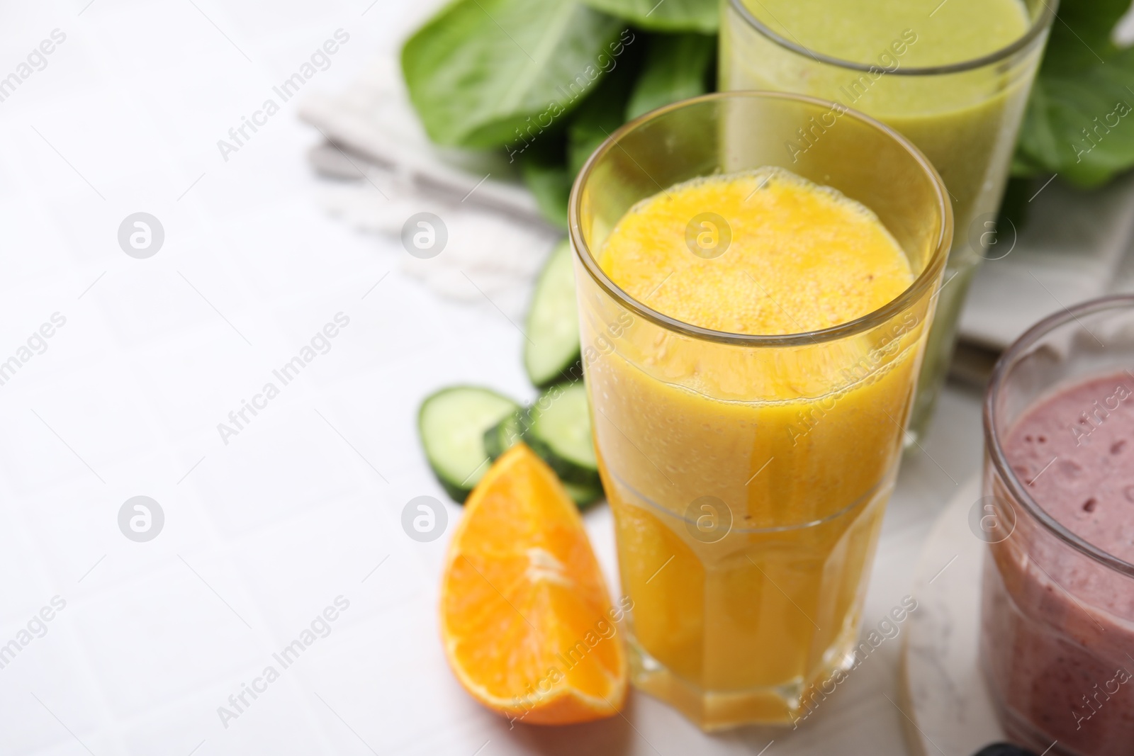 Photo of Tasty smoothies in glasses and ingredients on white tiled table, closeup. Space for text