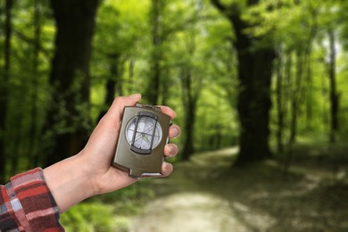 Image of Woman holding compass in green forest, closeup