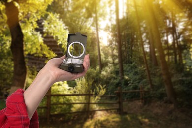 Woman holding compass near hut in sunlit forest, closeup