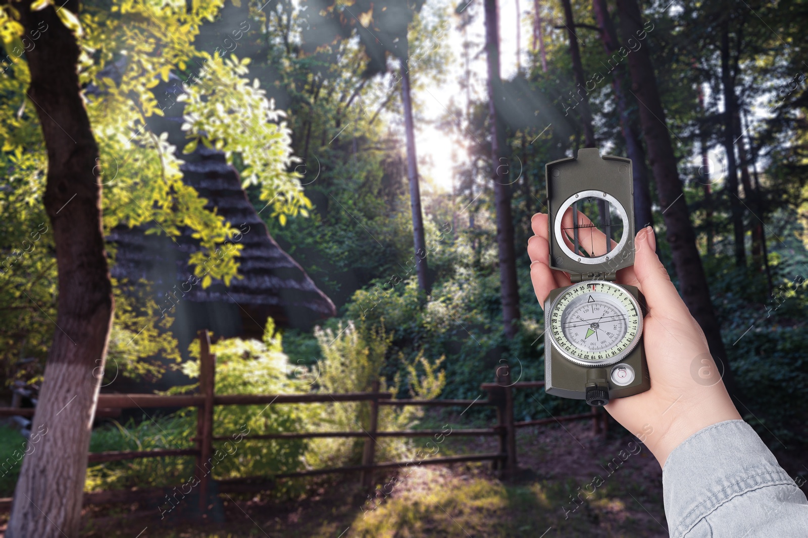 Image of Woman holding compass near hut in forest, closeup