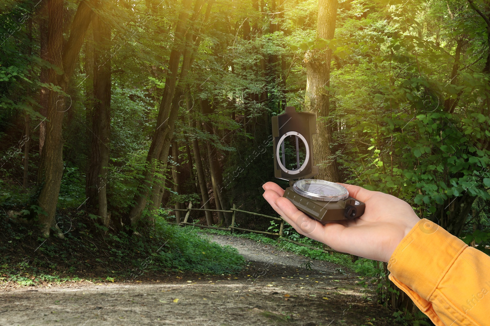 Image of Woman holding compass on pathway leading to forest, closeup