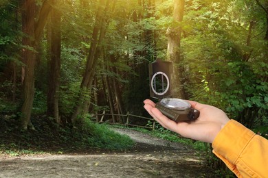 Image of Woman holding compass on pathway leading to forest, closeup