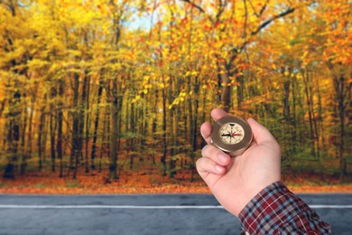 Image of Man holding compass near road going through forest in autumn, closeup