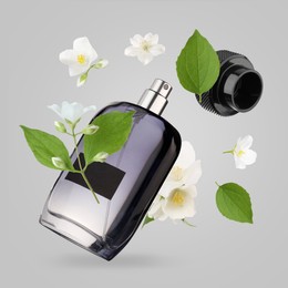 Bottle of floral perfume and jasmine flowers in air on light grey background