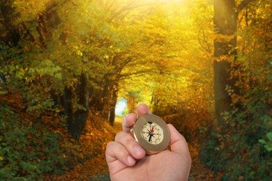 Image of Man holding compass on pathway in autumn forest, closeup