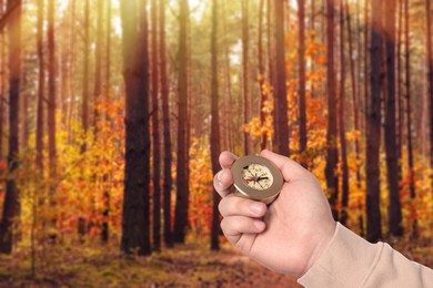 Image of Man holding compass in lush forest on autumn day, closeup