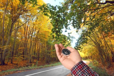 Image of Man holding compass near road going through forest in autumn, closeup