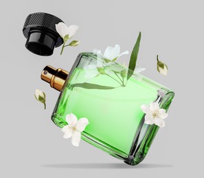 Bottle of floral perfume and jasmine flowers in air on light grey background