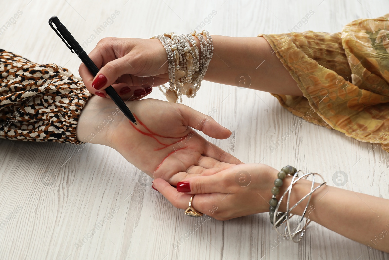 Photo of Fortune teller reading lines on woman's palm at white wooden table, closeup. Chiromancy