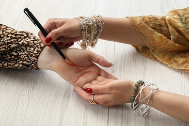 Fortune teller reading lines on woman's palm at white wooden table, closeup. Chiromancy