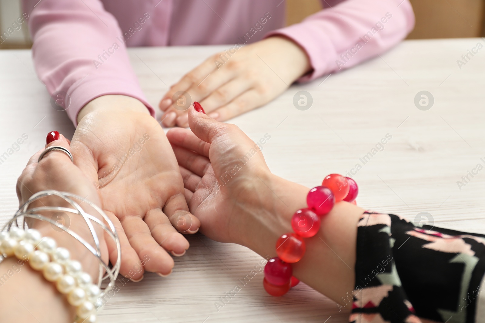 Photo of Fortune teller reading lines on woman's palm at white wooden table, closeup. Chiromancy