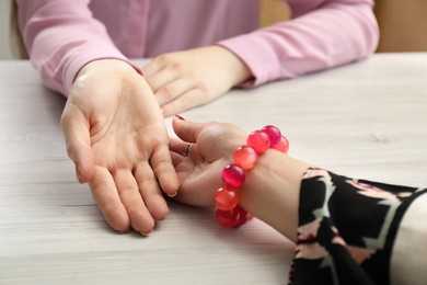 Fortune teller reading lines on woman's palm at white wooden table, closeup. Chiromancy