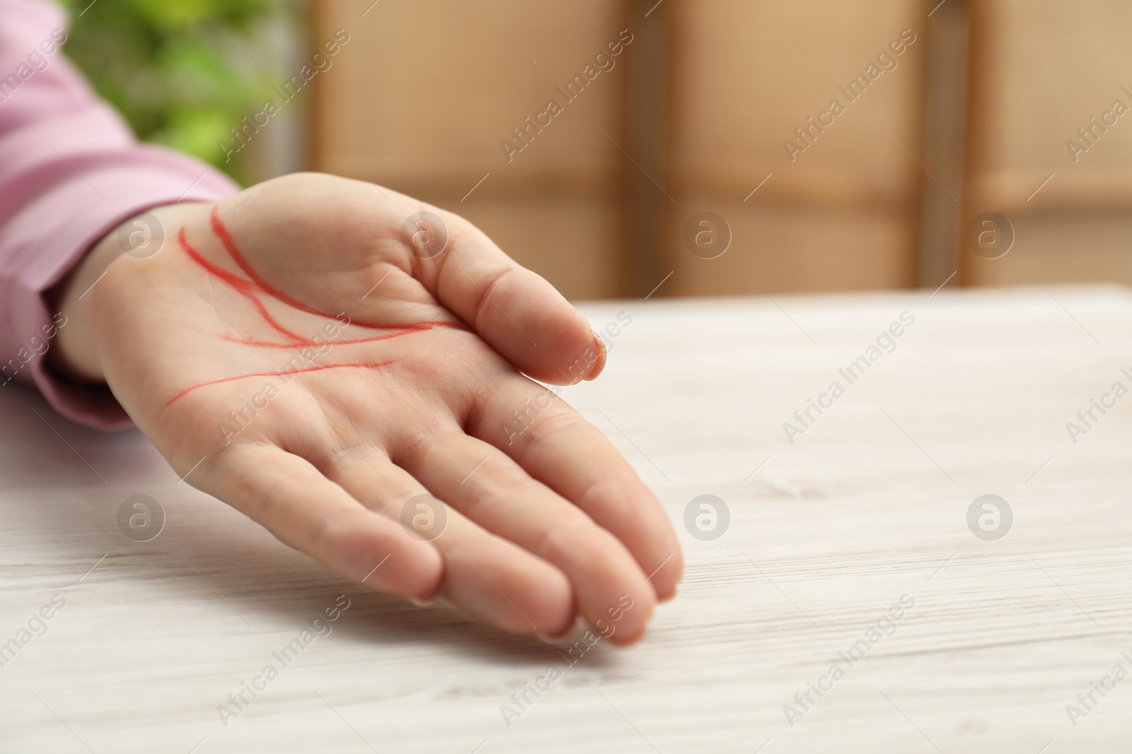 Photo of Chiromancy and foretelling. Woman showing palm with drawn lines at white wooden table, closeup. Space for text